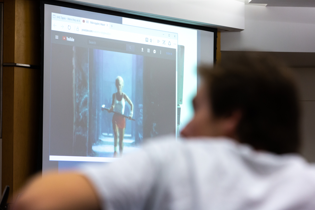 Blurred image of a student from behind watching a film projected onto a large screen